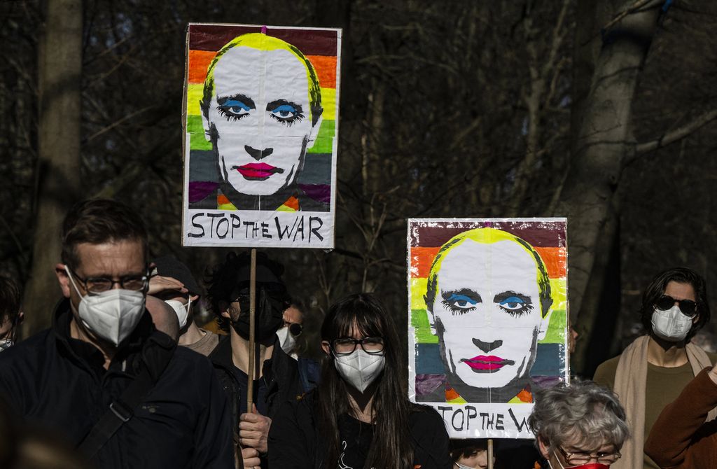 Para pengunjuk rasa membawa poster bergambar wajah Presiden Rusia Vladimir Putin yang diubah, dalam demonstrasi menentang invasi Rusia ke Ukraina, di Berlin, Jerman, Minggu (13/3/2022).
