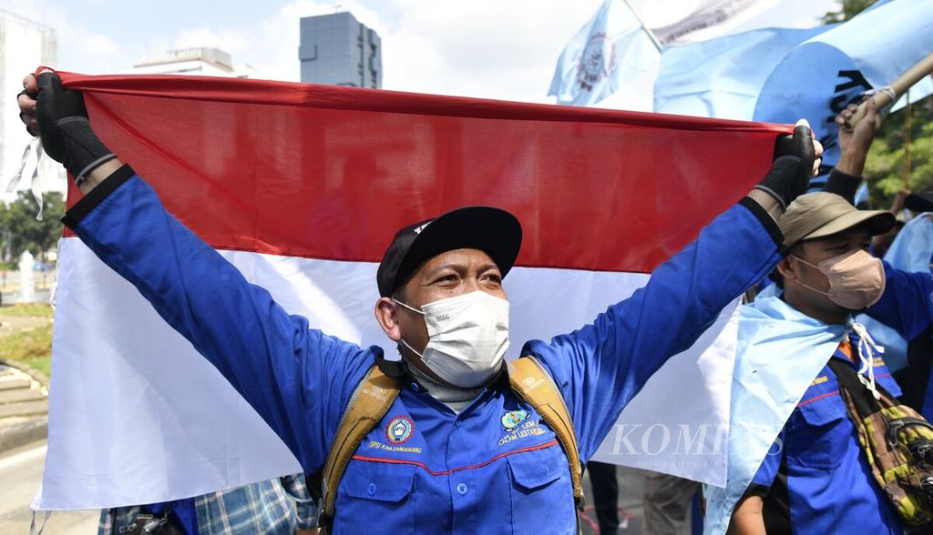Salah seorang peserta aksi membentangkan bendera Merah Putih saat mengikuti unjuk rasa buruh di kawasan bundaran Patung Arjuna Wijaya, Jakarta Pusat, Kamis (12/5/2022). Aksi yang diikuti massa buruh dari Konfederasi Serikat Pekerja Seluruh Indonesia (KSPSI) itu merupakan peringatan Hari Buruh (May Day) pada 1 Mei lalu yang tertunda karena menjelang hari raya Idul Fitri. Dalam aksinya, para buruh menyerukan empat tuntutan untuk perbaikan kesejahteraan pekerja.