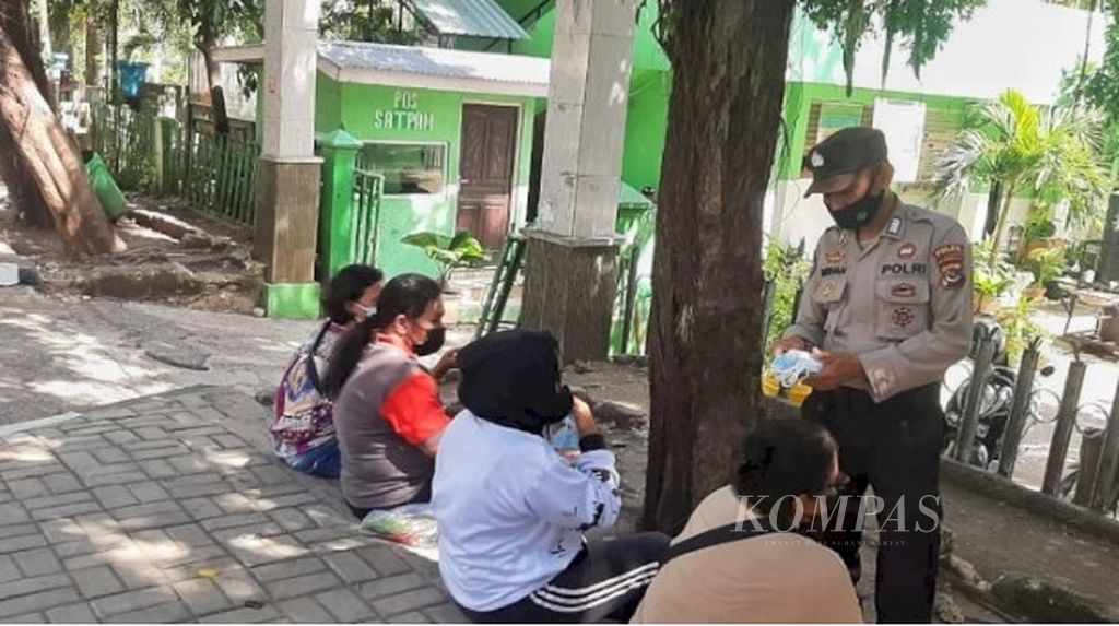 Seorang anggota Polda NTT melakukan sosialisasi penerapan protokol kesehatan kepada warga Kupang yang sedang nongkrong di jalan dan trotoar. Mereka membagikan masker kepada warga dan mengajak warga menjaga jarak.