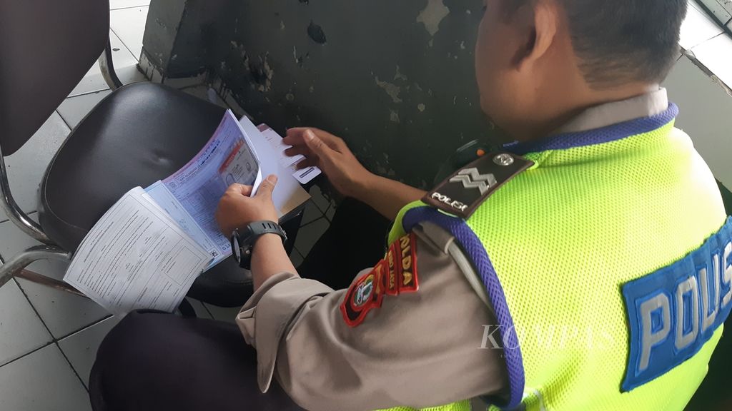 Seorang polisi sedang mengecek surat tilang pelanggar aturan ganjil genap di pos polisi, di Jalan Salemba Raya, Jakarta Pusat. Data pelanggar dalam surat itu diunggah ke platform tilang elektronik. Senin (13/6/2022), polisi mulai menerapkan sanksi bagi pelanggar aturan tersebut.