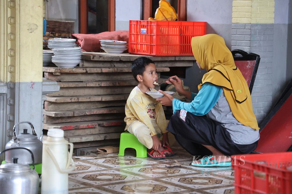 Ibu rumah tangga mengasuh anak sambil bergotong royong menyiapkan makanan dan minuman untuk suguhan saat acara peringatan ulang tahun ke-60 kelompok seni soreng Warga Setuju di Desa Bandungrejo, Ngablak, Magelang, Jawa Tengah, Jumat (4/8/2023). 