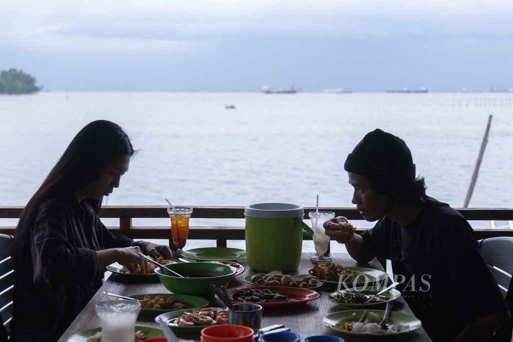 Warga menyantap hidangan boga bahari sambil menikmati pemandangan Selat Singapura di rumah makan seafood Gerai Nelayan 2M di Kampung Tua Mentarau, Kecamatan Sekupang, Batam, Kepulauan Riau, Sabtu (29/4/2023).