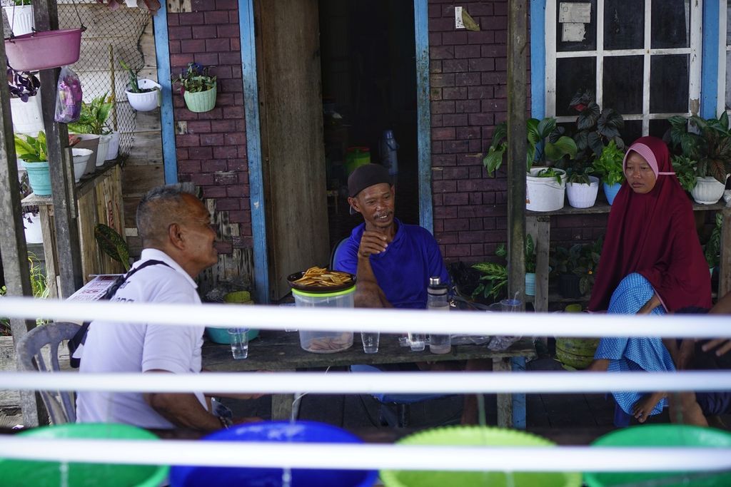 Mahmud (60), Syaiful (52), dan Titin (40) sedang berbincang di depan rumah di Kelurahan Jenebora, Kecamatan Penajam, Penajam Paser Utara, Kalimantan Timur, Minggu (6/3/2022). Mereka kesulitan mendapat minyak goreng meskipun rumah mereka terletak di seberang pabrik pengolahan minyak sawit di muara Teluk Balikpapan.