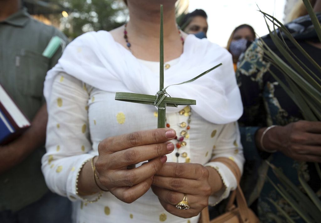 Umat Katolik membawa daun palem yang dibentuk menjadi salib pada perayaan Minggu Palem di Karachi, Pakistan, Minggu (10/4/2022). 