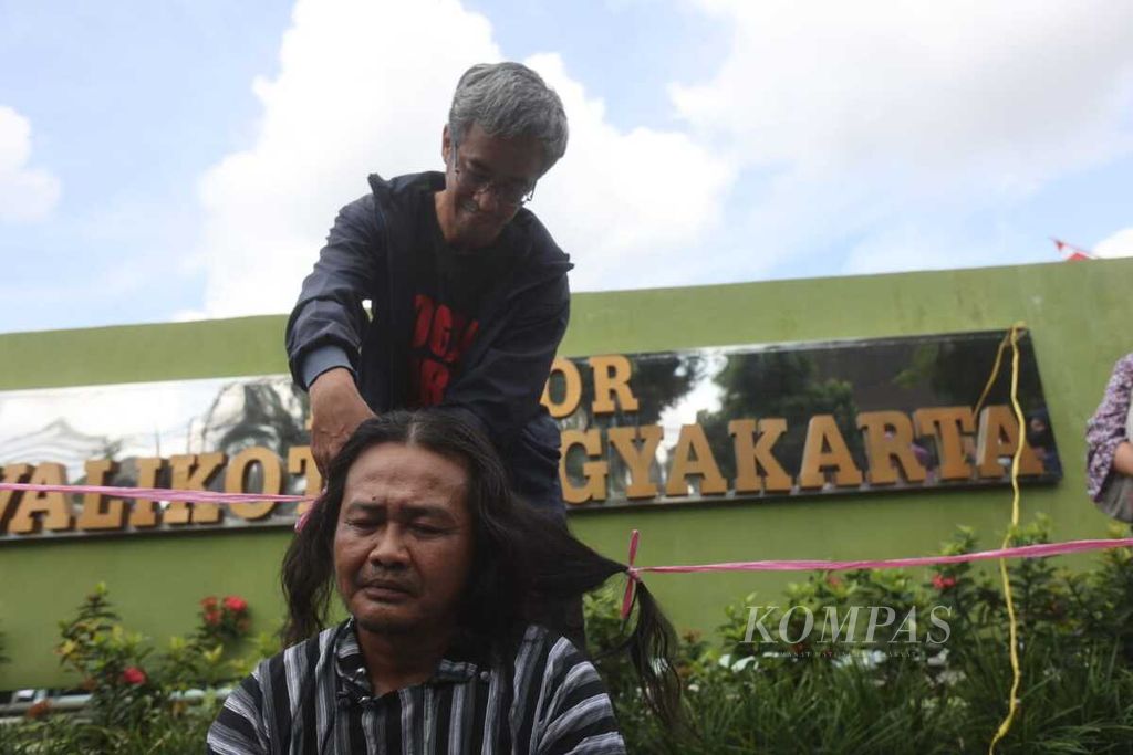 Seorang warga memotong rambut aktivis asal Yogyakarta, Dodo Putra Bangsa, dalam aksi cukur gundul di depan Balai Kota Yogyakarta, Sabtu (4/6/2022). 