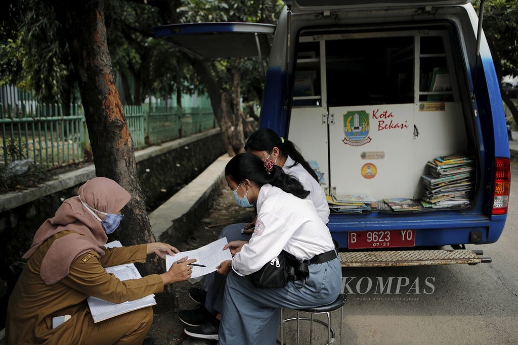Dua siswi SMKN 3 Kota Bekasi yang magang memperhatikan catatan peminjaman buku di belakang mobil perpustakaan keliling dari Dinas Arsip dan Perpustakaan Daerah Kota Bekasi yang diparkir di Jalan Guntur Raya, Kota Bekasi, Jawa Barat, Senin (14/6/2021).