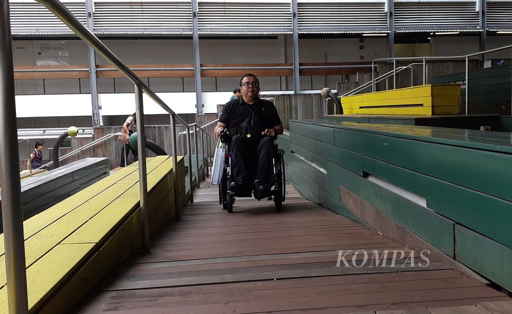 Pemandu dari Tribe Tours, Warren Sheldon Humphries, menggunakan kursi roda di Enabling Village, Singapura, Selasa (10/10/2023). Kawasan ini merupakan ruang komunitas inklusif yang mempunyai beragam fasilitas, seperti <i>gym</i>, pusat inovasi teknologi, galeri, pusat perbelanjaan, dan fasilitas lain yang ramah terhadap penyandang disabilitas.