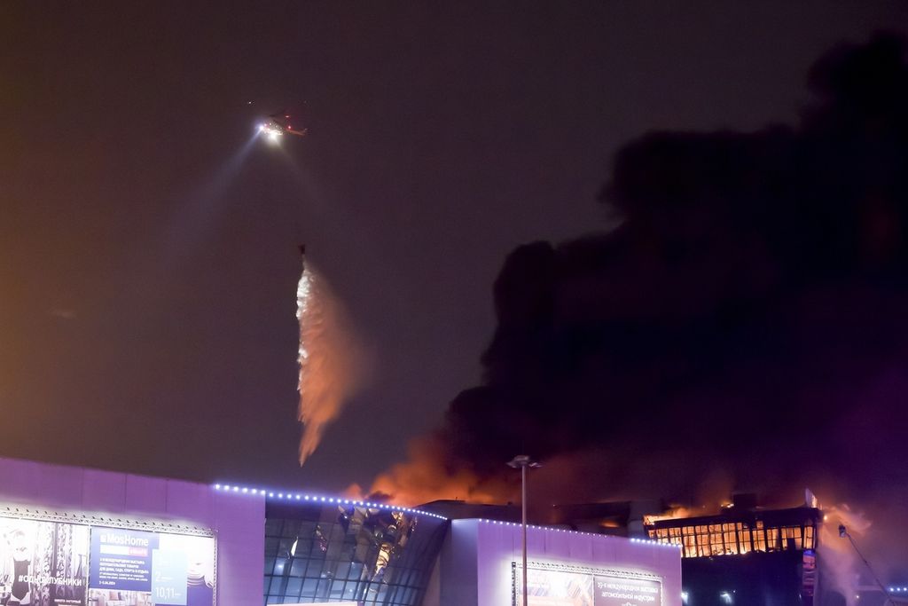Sebuah helikopter berupaya memadamkan kobaran api di Crocus City Hall di pinggiran barat Moskwa, Rusia, Jumat (22/3/2024). 