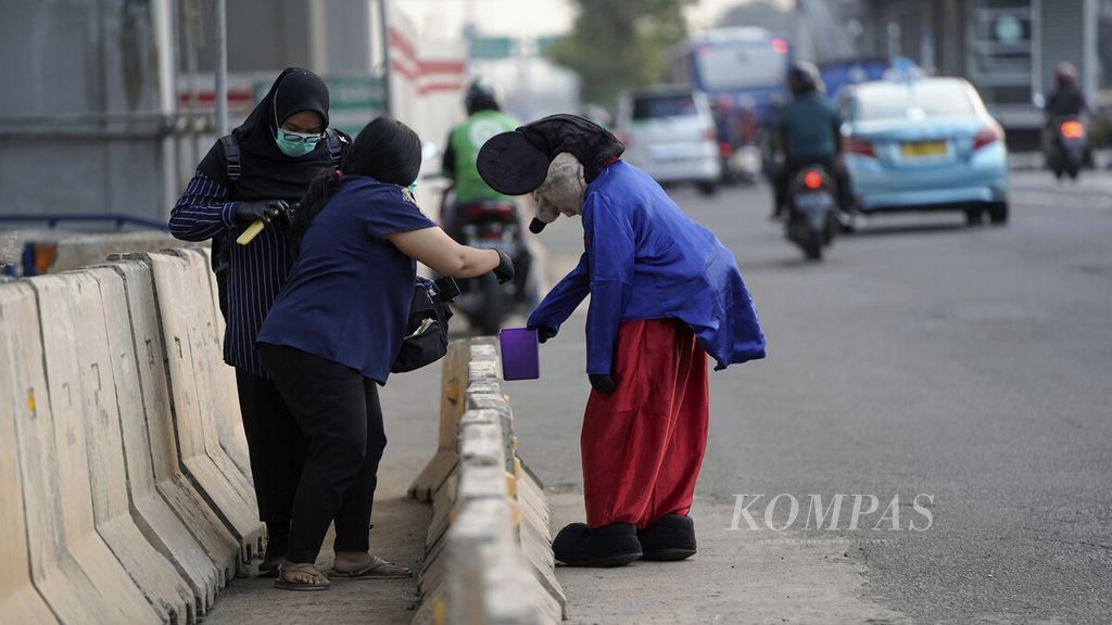 Pejalan kaki memberi uang kepada badut Mickey Mouse yang berjalan gontai di Jalan MT Haryono, Jakarta, Rabu (8/7/2020).