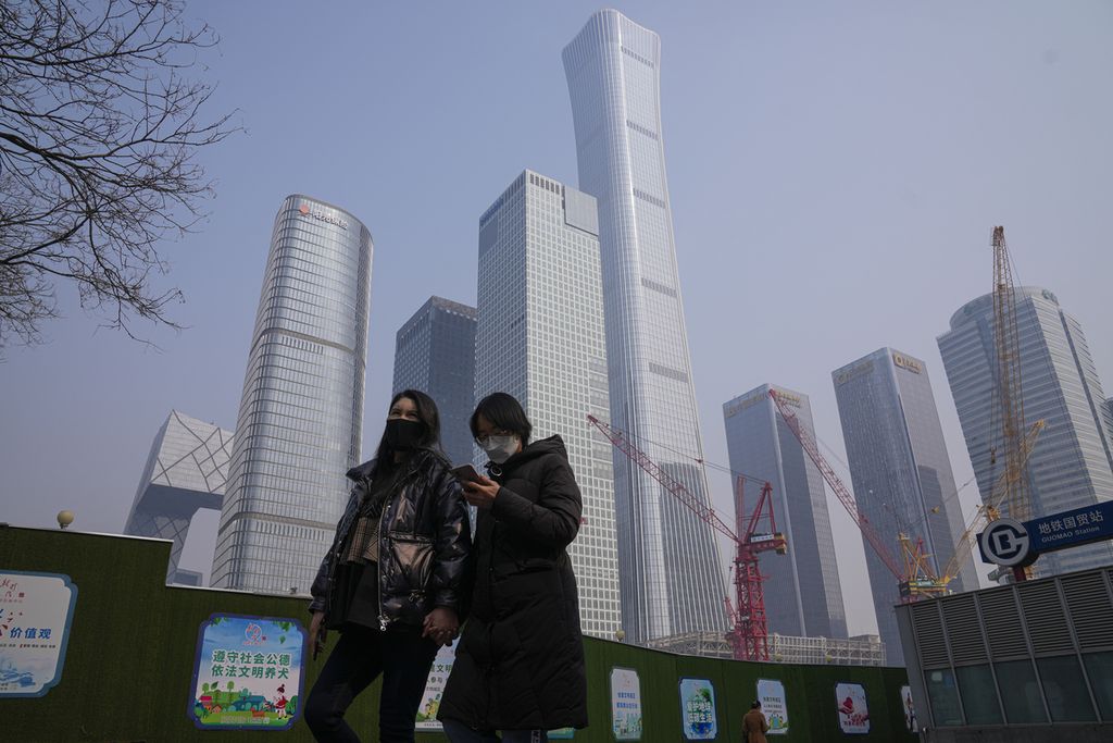 Perempuan yang mengenakan masker berjalan di dekat poster propaganda pemerintah di dekat konstruksi di kawasan pusat bisnis di Beijing pada 27 Februari 2023. 