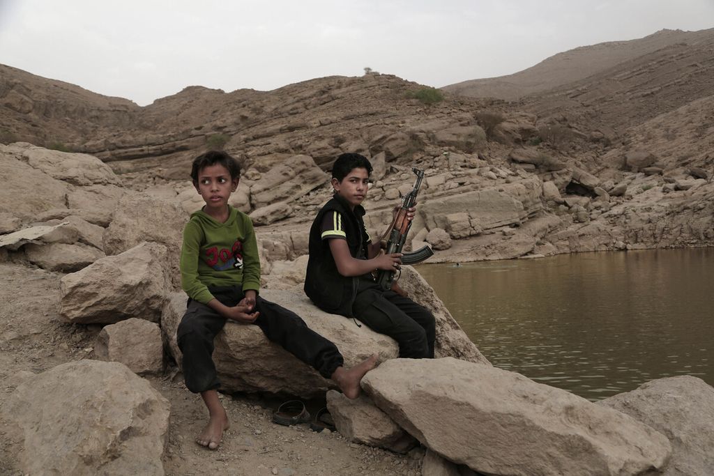 Dua petempur anak-anak yang baru berusia remaja duduk di bebatuan sambil membawa senjata api di sebuah lokasi di Marib, Yaman, 30 Juli 2018. Sudah bertahun-tahun negara itu dilanda perang saudara dan tidak ada tanda akan selesai. Perang Yaman salah satu bukti perpecahan di antara bangsa Arab.