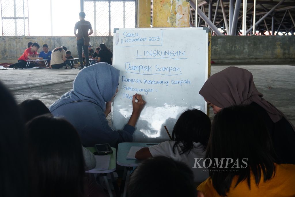 Nuraini Adariku (19), sukarelawan di Komunitas Dinding Manado, menulis bahan ajar di papan tulis dalam kegiatan kelas informal mingguan yang diselenggarakan komunitas tersebut di lantai 3 gedung utama Pasar Bersehati, Sabtu (11/11/2023). 