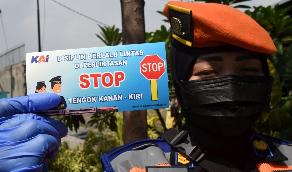 Petugas PT KAI Daop 8 menunjukkan stiker yang akan dibagikan kepada pengendara saat sosialisasi keselamatan di pelintasan sebidang di Perlintasan Kereta Api Jalan Ahmad Yani, Surabaya, Jawa Timur, (14/10/2020).