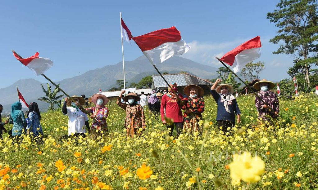 Warga mengibarkan bendera merah putih seusai Upacara HUT ke-76 Kemerdekaan RI di tengah kebun bunga refugia, Desa , Kecamatan Trawas, Kabupaten Mojokerto, Jawa Timur, Selasa (17/8/2021). Upacara diikuti oleh warga anggota Komunitas Pertanian Organik Brenjonk.  
