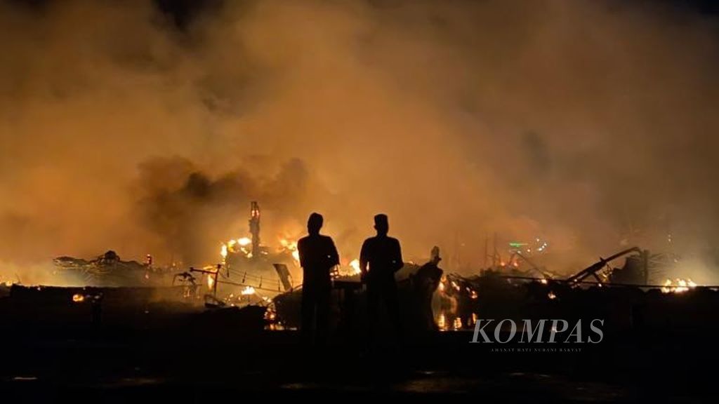 Residents observe the site of a fire that engulfed dozens of fishing boats at the Tegalsari Beach Fishing Port, West Tegal District, Tegal City, Central Java, Tuesday morning (15/8/2023). Until ten hours after the incident, the fire that occurred since Monday (14/8/2023) night has not been extinguished.