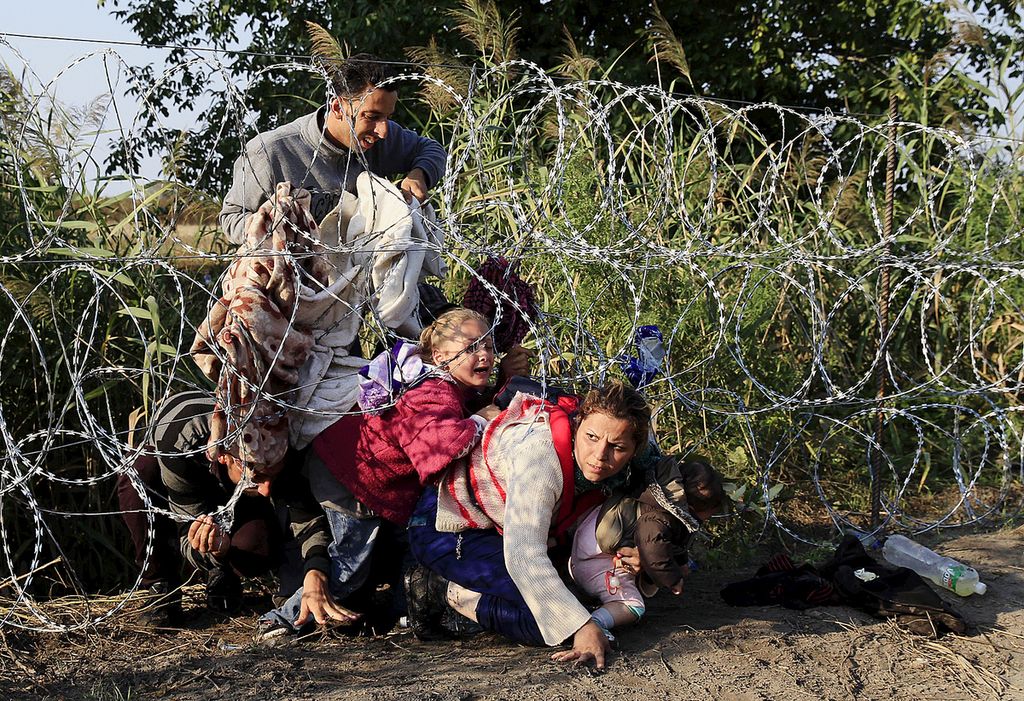 Pengungsi Suriah menyelinap di bawah pagar kawat berduri di Roszke, Hongaria pada 27 Agustus 2015.    