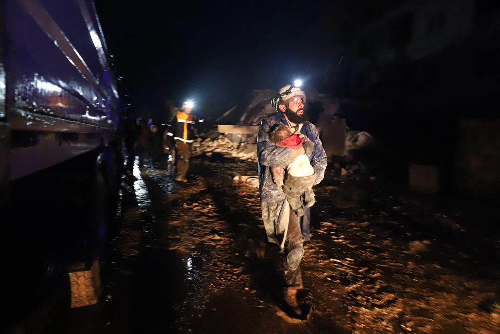 Seorang laki-laki anggota White Helmet membawa balita yang berhasil diselamatkan dari reruntuhan bangunan di Zardania, sebuah kota kecil di Provinsi Idlib, Suriah, Senin (6/2/2023). Gempa bermagnitudo 7,8 yang mengguncang Turki dan Suriah diperkirakan menelan korban lebih dari 5.000 jiwa. 