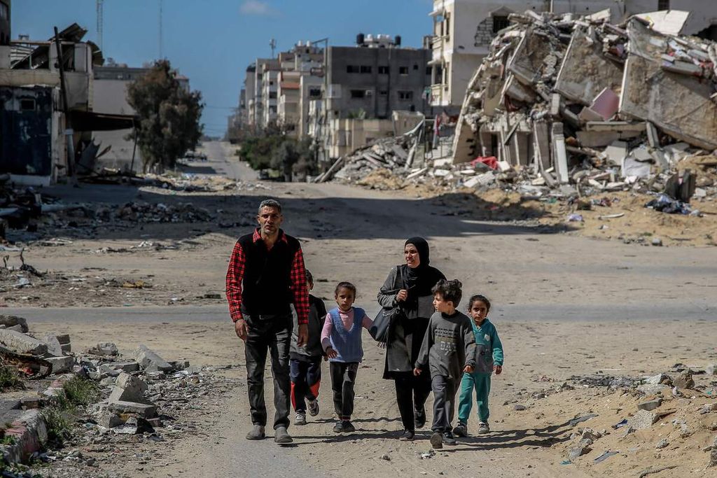 Satu keluarga warga Palestina berjalan melewati puing-puing gedung yang hancur akibat serangan Israel sebelumnya di kota Gaza, Senin (25/3/2024). 