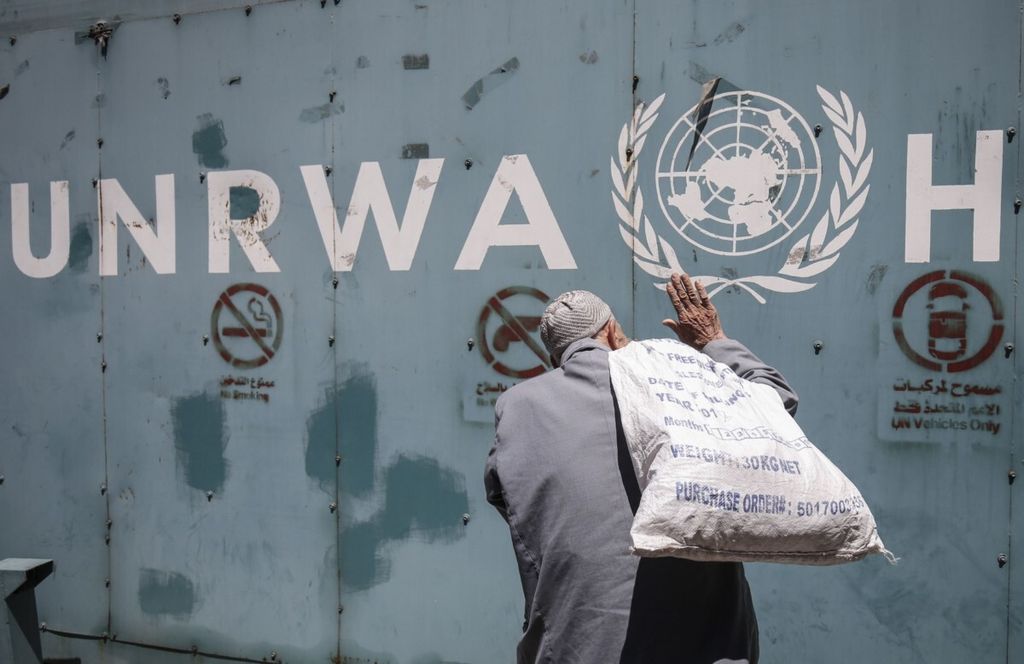 Seorang pria Palestina berdiri di depan emblem Badan PBB untuk Pemulihan dan Kerja bagi Pengungsi Palestina di Timur Dekat (UNRWA) di luar kantor lembaga tersebut di Gaza City, 31 Juli 2018.  