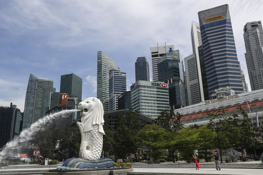 Warga tampak mengambil foto di dekat patung Merlion dengan latar belakang gedung-gedung perkantoran di kawasan Marina Bay, Singapura, 30 Juni 2020. 