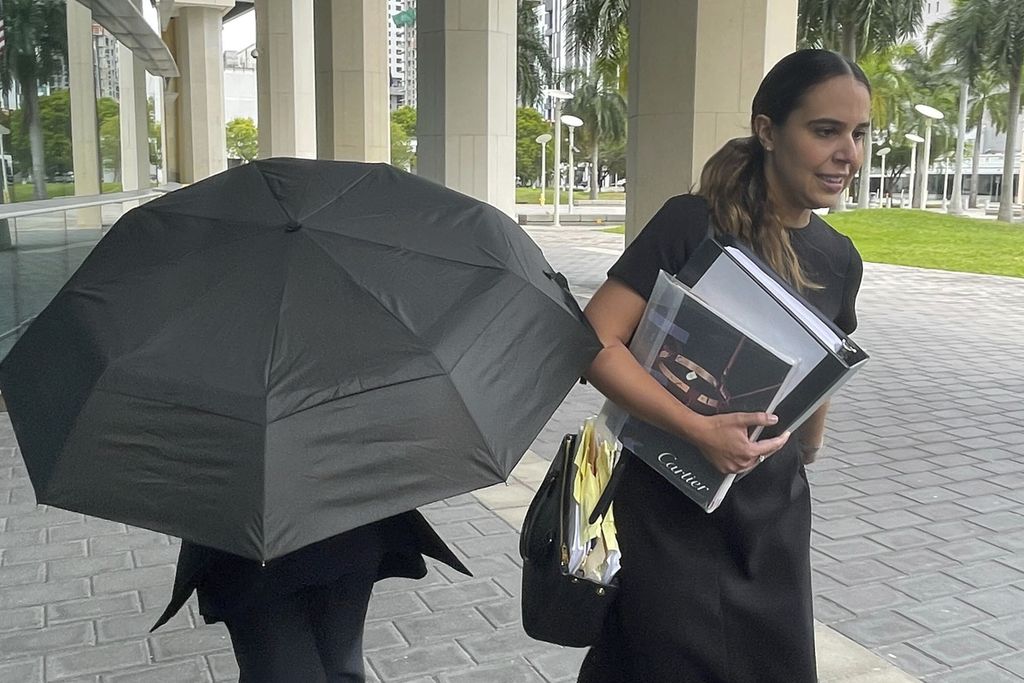 Perancang Nancy Gonzalez bersembunyi di balik payung dan pengacaranya Andrea Lopez (kanan) kala tiba di Pengadilan Miami, Florida, Senin (22/4/2024)