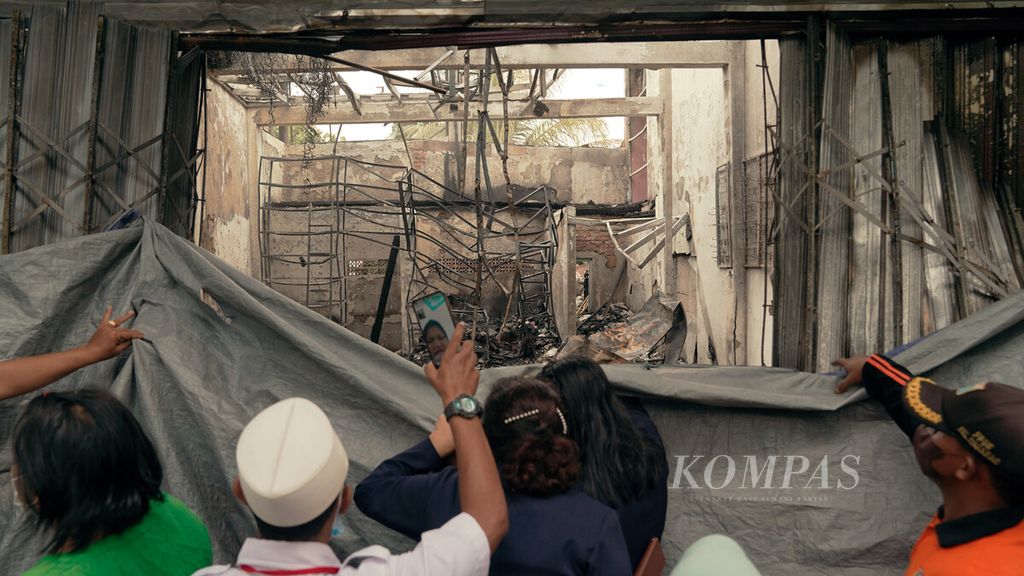 Rumah toko berupa bengkel motor di Jalan Warakas 1, Tanjung Priok, Jakarta Utara, Selasa (12/4/2022), yang hangus terbakar dibatasi terpal. Namun, sebagian warga tetap berupaya mengintip ke dalam untuk melihat konsisi ruko.