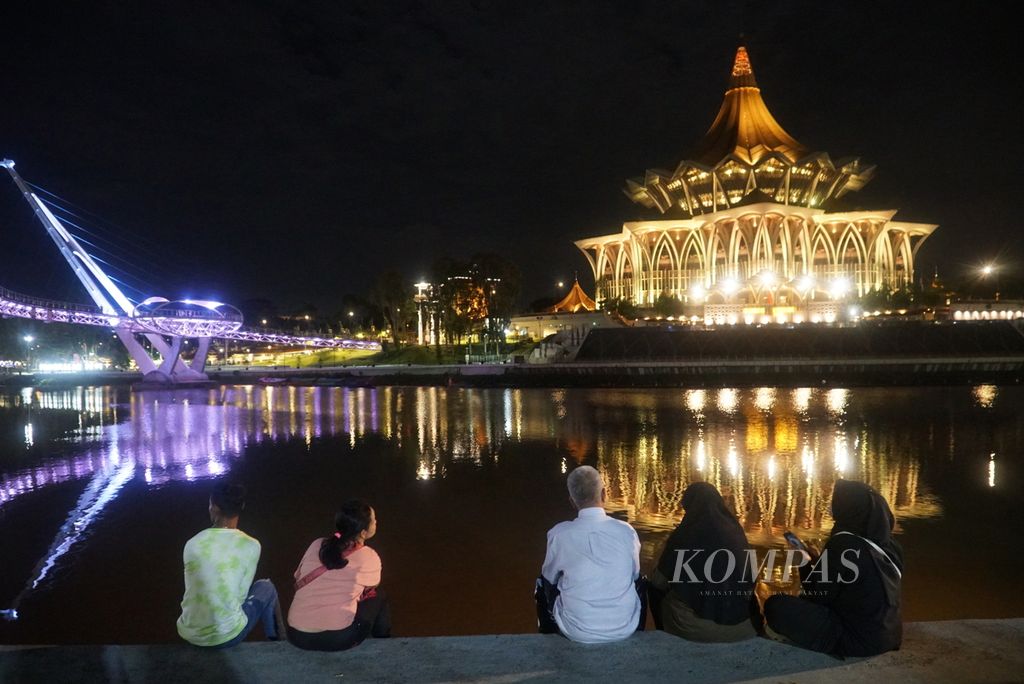 Pengunjung menikmati pemandangan malam di Kuching Waterfront yang berhadapan dengan Gedung Dewan Undangan Negeri Sarawak (kanan) dan Jembatan Darul Hana (kiri) di seberang Sungai Sarawak, kota Kuching, Sarawak, Malaysia, Kamis (22/2/2024) malam. 