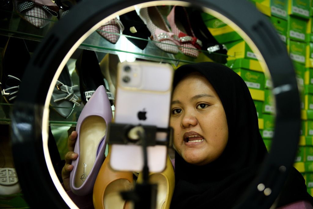 Pedagang menawarkan sepatu kepada para pengguna media sosial Tiktok saat siaran langsung di kios Blok A Tanah Abang, Jakarta, Selasa (13/6/2023). Penjualan secara daring menjadi salah satu strategi para pedagang untuk menjangkau konsumen yang lebih luas. 