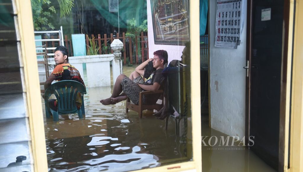 Warga berada di depan rumahnya saat banjir di Jalan Kenari, Kecamatan Sampang, Kabupaten Sampang, Jawa Timur, Senin (2/1/2023). 
