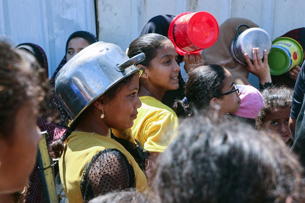 Anak-anak Palestina mengantre sambil membawa peralatan makan mereka di titik distribusi makanan di kamp pengungsi Jabalia di Jalur Gaza utara, Rabu (21/8/2024).