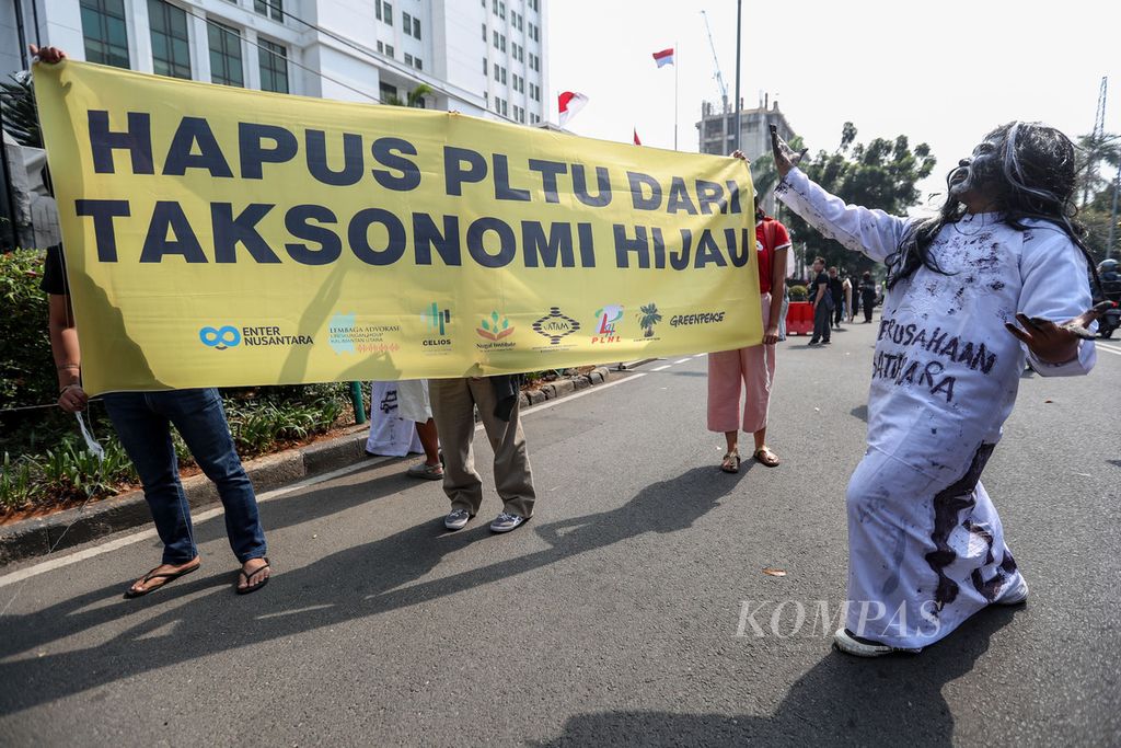 Peserta aksi membentangkan spanduk berisi pesan aksi di depan kantor Otoritas Jasa Keuangan (OJK) Gedung Sumitro Djojohadikusumo, Jakarta, Jumat (15/9/2023).  