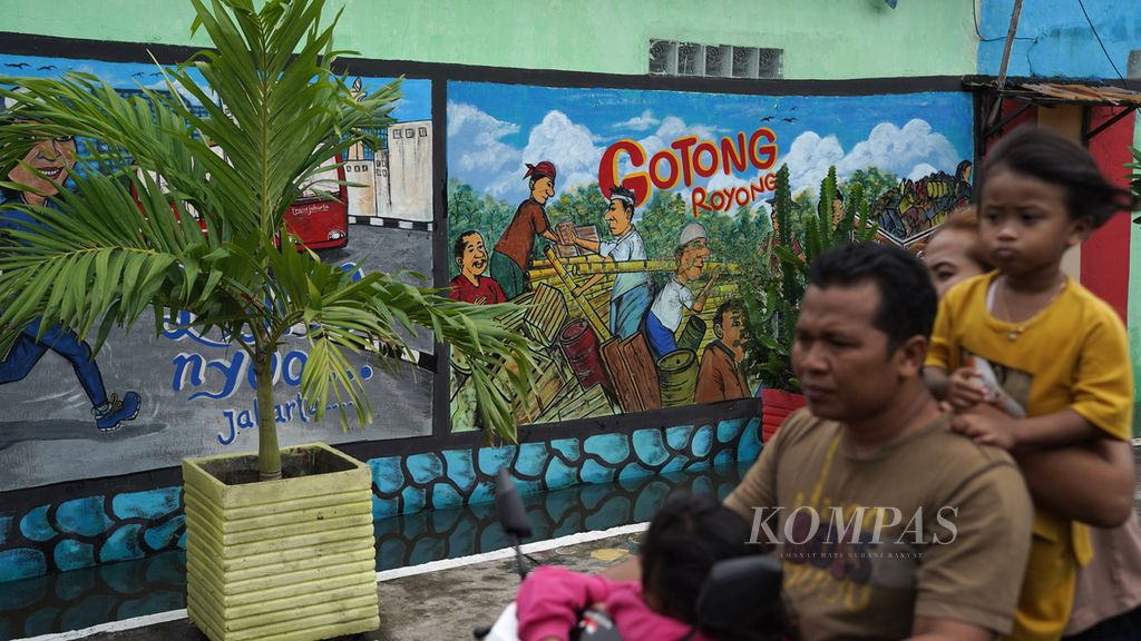 Warga melintasi mural ajakan melestarikan gotong royong dalam kehidupan sehari-hari di Kelurahan Lagoa, Kecamatan Koja, Jakarta Utara, Minggu (1/1/2023). 