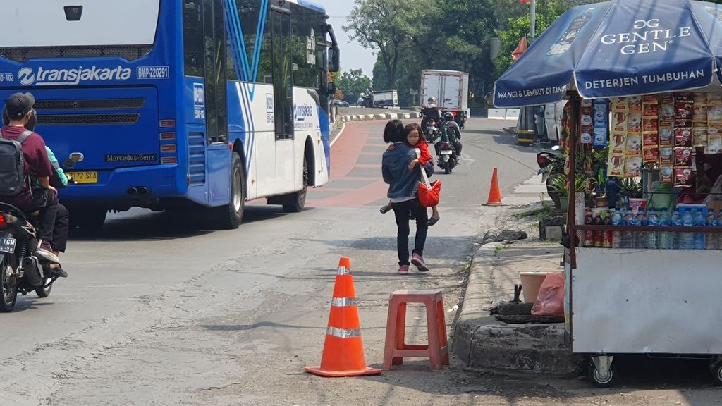 Seorang warga melintas di jalan raya Jakarta-Bogor menuju Terminal Lebak Bulus, Cilandak, Jakarta Selatan, pada Selasa (16/5/2023). Dia harus berbagi jalan dengan kendaraan bermotor karena tidak ada trotoar yang memadai.