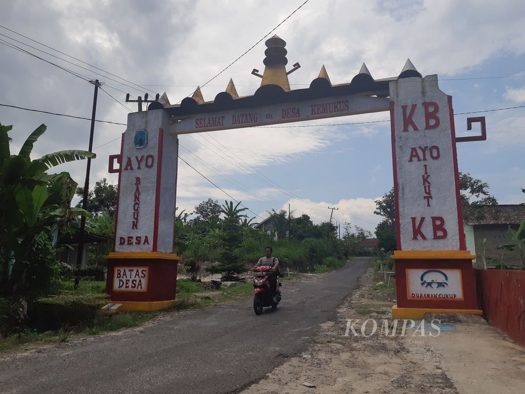 Seorang warga melewati gapura Desa Kemukus, Kecamatan Ketapang, Kabupaten Lampung Selatan, Lampung, pada Selasa (9/1/2024). Desa tersebut masuk dalam kawasan hutan produksi Register 1 Way Pisang.