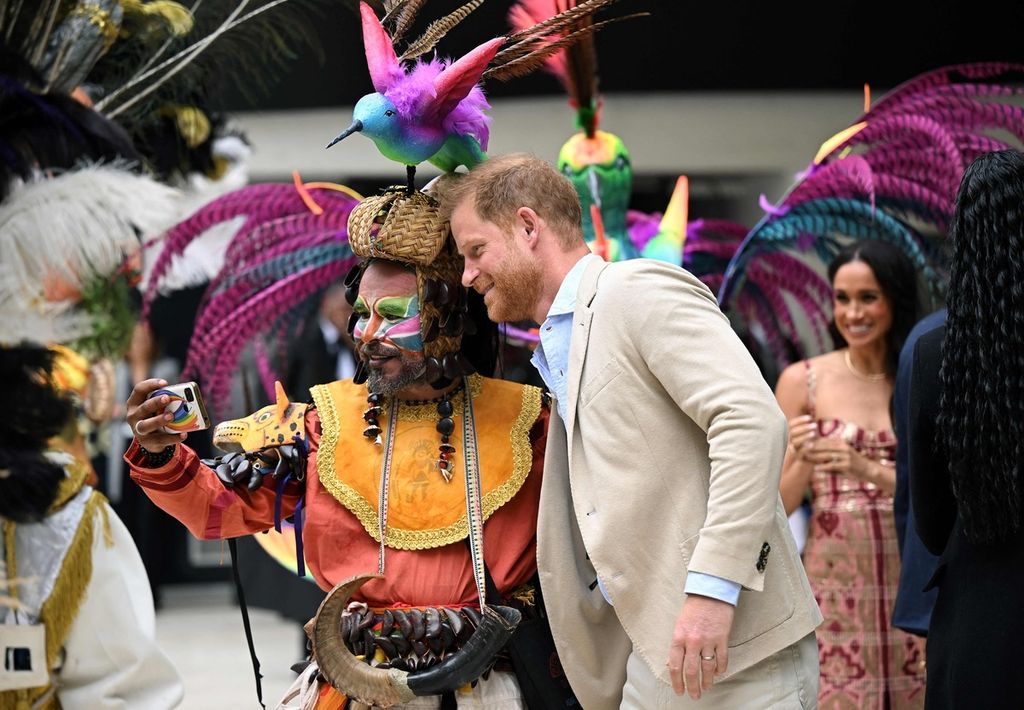 Pangeran Harry berpose untuk swafoto dengan seorang seniman, sementara istrinya, Meghan (kanan), memperhatikan selama kunjungan di Pusat Seni Nasional di Bogota, Kolombia, 15 Agustus 2024.  