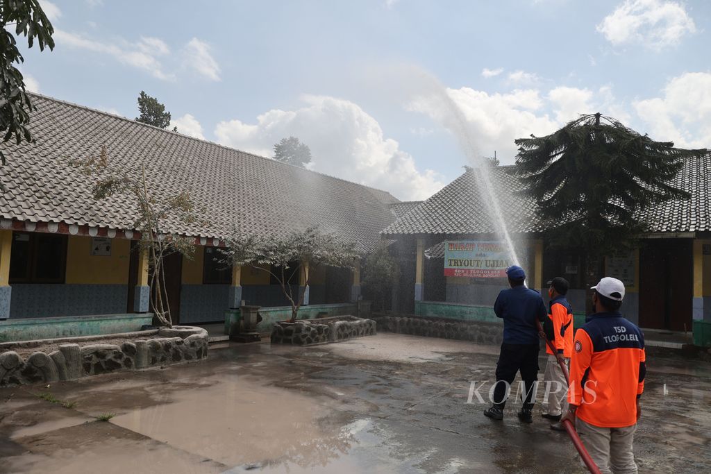 Petugas BPBD Boyolali menyemprotkan air untuk membersihkan abu vulkanik di kompleks SD Negeri 1 Tlogolele, Desa Tlogolele, Selo, Boyolali, Jawa Tengah, Senin (13/3/2023). 