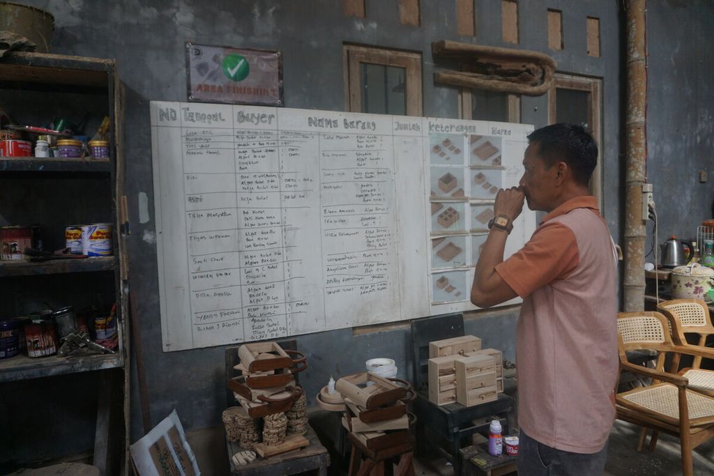 Suhendi (46) melihat daftar pesanan kerajinan kayu dari limbah di bengkel kerjanya di Desa Majatengah, Kecamatan Kemangkon, Kabupaten Purbalingga, Jawa Tengah, Rabu (25/1/2023).