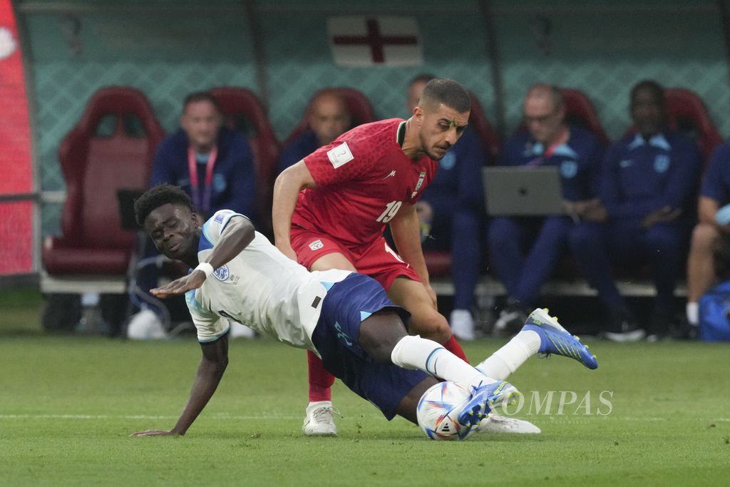 Pemain Inggris, Bukayo Saka, terjatuh saat berebut bola dengan pemain Iran di babak penyisihan Grup B Piala Dunia Qatar 2022 di Stadion Khalifa, Qatar, Senin (21/11/2022). Inggris menang 6-2 atas Iran. 