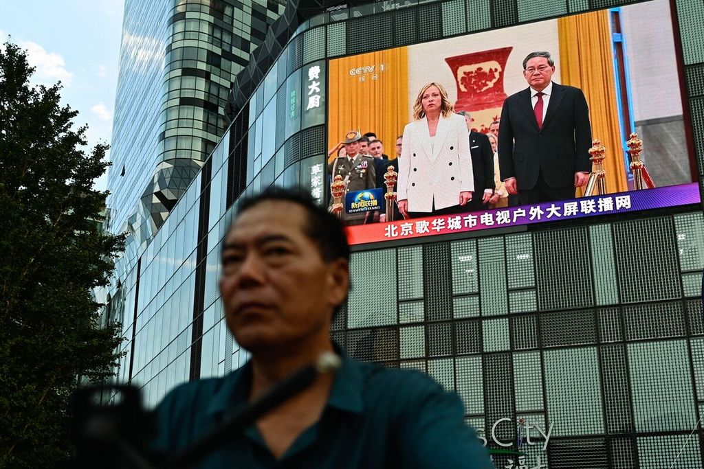 Warga Beijing, China, berjalan di depan layar raksasa yang menampilkan Perdana Menteri Li Qiang (kanan) dan PM Italia Giorgia Meloni, Minggu (28/7/2024).