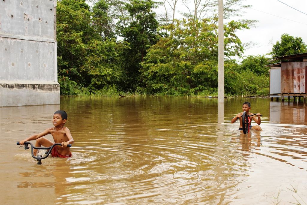 Anak-anak bermain sepeda ketika banjir di wilayah Pahandut Seberang, Kota Palangkaraya, Kalteng, Minggu (14/11/2021). Banjir di Kalteng merendam setidaknya beberapa wilayah di empat kabupaten dan kota. Menurut pemerintah, banjir disebabkan cuaca ekstrem.