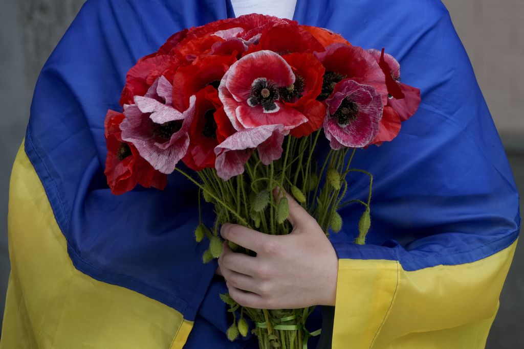 Seorang perempuan berselimut bendera Ukraina memegang bunga saat berlangsung upacara pemakaman seorang tentara di Kyiv, Ukraina, 18 Juni 2022. 
