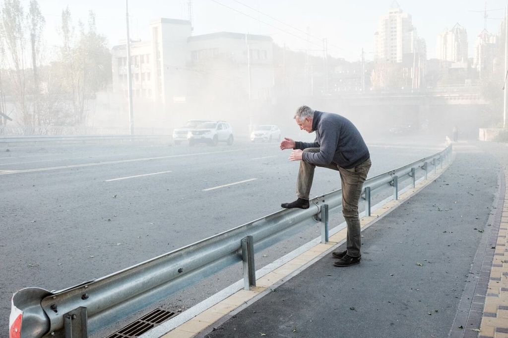 Seorang pria berusaha membersihkan debu yang ditimbulkan ledakan serangan pesawat tak berawak di Kyiv, Ukraina, Senin (17/10/2022). Pada Senin pagi waktu setempat, sedikitnya telah terjadi empat kali ledakan.