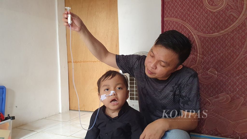 Tay David Sulu (36) memangku anaknya, Alvaro (4), yang masih berjuang untuk sembuh setelah mengalami gangguan ginjal akut progresif atipikal, Minggu (9/7/2023).