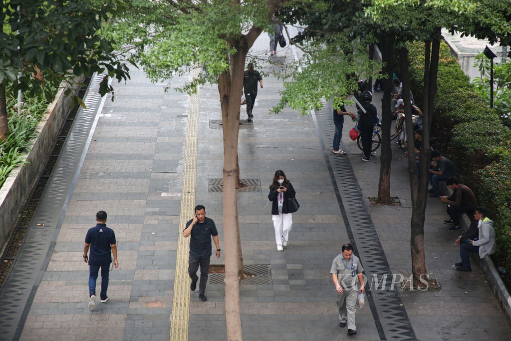 Employees walk along the pedestrian pathway on Jenderal Sudirman Street, Jakarta, during their lunch break on Tuesday (21/11/2023).