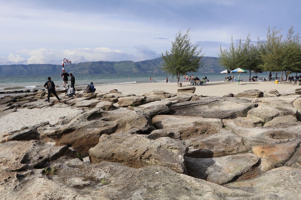 Wisatawan menikmati keindahan Danau Toba di Pantai Batu Hoda, Kecamatan Simanindo, Kabupaten Samosir, Sumatera Utara, Minggu (10/10/2021). Batu dan pasir di kawasan itu terangkat dari kedalaman 500 meter bersama Pulau Samosir 37.000 sampai 40.000 tahun lalu. 