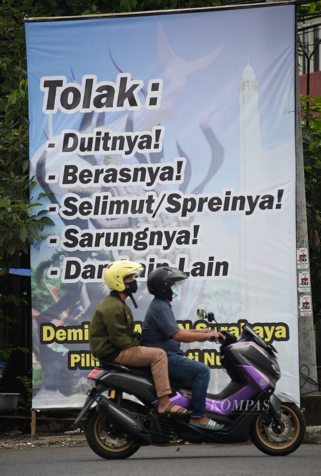 Warga melintasi spanduk anjuran untuk menolak pemberian dalam Pilkada Kota Surabaya di Jalan Kombes Pol M Duriyat, Surabaya, Jawa Timur, Senin (7/12/2020). Hal tersebut dilakukan untuk menciptakan pilkada yang bermartabat.