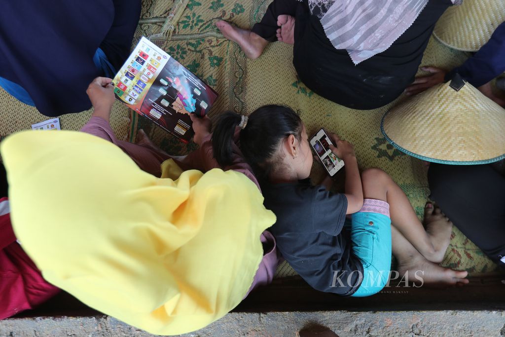 Seorang anak bermain ponsel di tengah sosialisasi Pemilu 2024 kepada warga Kecamatan Mojogedang, Kabupaten Karanganyar, Jawa Tengah, Kamis (28/9/2023).
