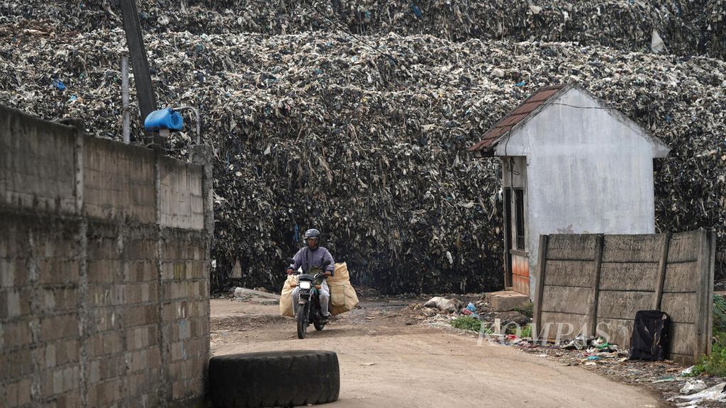 Warga melewati pagar batas tumpukan sampah di Tempat Pengelolaan Sampah Terpadu (TPST) Bantargebang di Kota Bekasi, Jawa Barat, Kamis (19/1/2023). Tumpukan sampah semakin menggunung di TPST Bantargebang. Setiap hari ada 1.200 truk mengangkut sekitar 7.500 ton sampah dari Jakarta. 