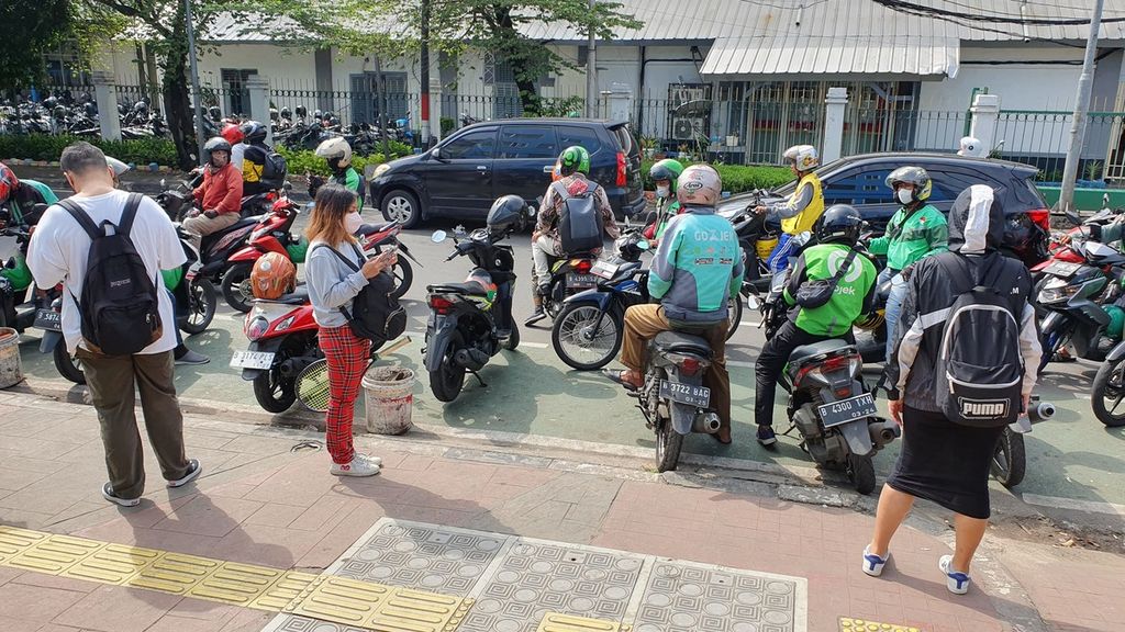 Sejumlah warga menunggu ojek daring dari pinggir Jalan Palmerah Timur atau tepatnya di sisi barat Stasiun Palmerah, Kelurahan Gelora, Kecamatan Tanah Abang, Jakarta Pusat, Selasa (9/5/2023). Titik penjemputan ini mengakibatkan kemacetan yang selalu terjadi pada waktu berangkat dan pulang kerja.