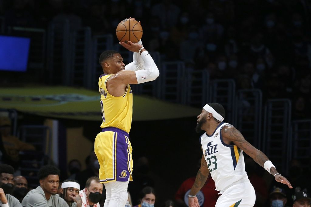 Pemain Los Angeles Lakers Russell Westbrook (kiri) melempar bola setelah melewati adangan pemain Utah Jazz Royce O'Neale, pada paruh pertama laga NBA di Arena Crypto.com, Los Angeles, Senin (17/1/2022)